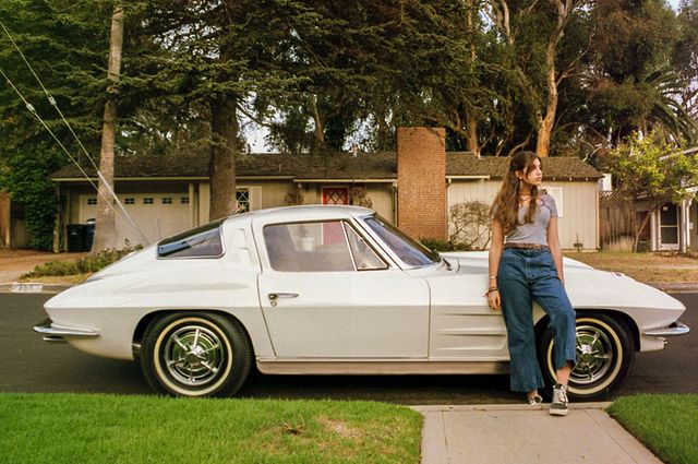 Shana Leelee Chasman in a light blue t-shirt and blue jeans posing in front of her Chevrolet Corvette C2 Z06.